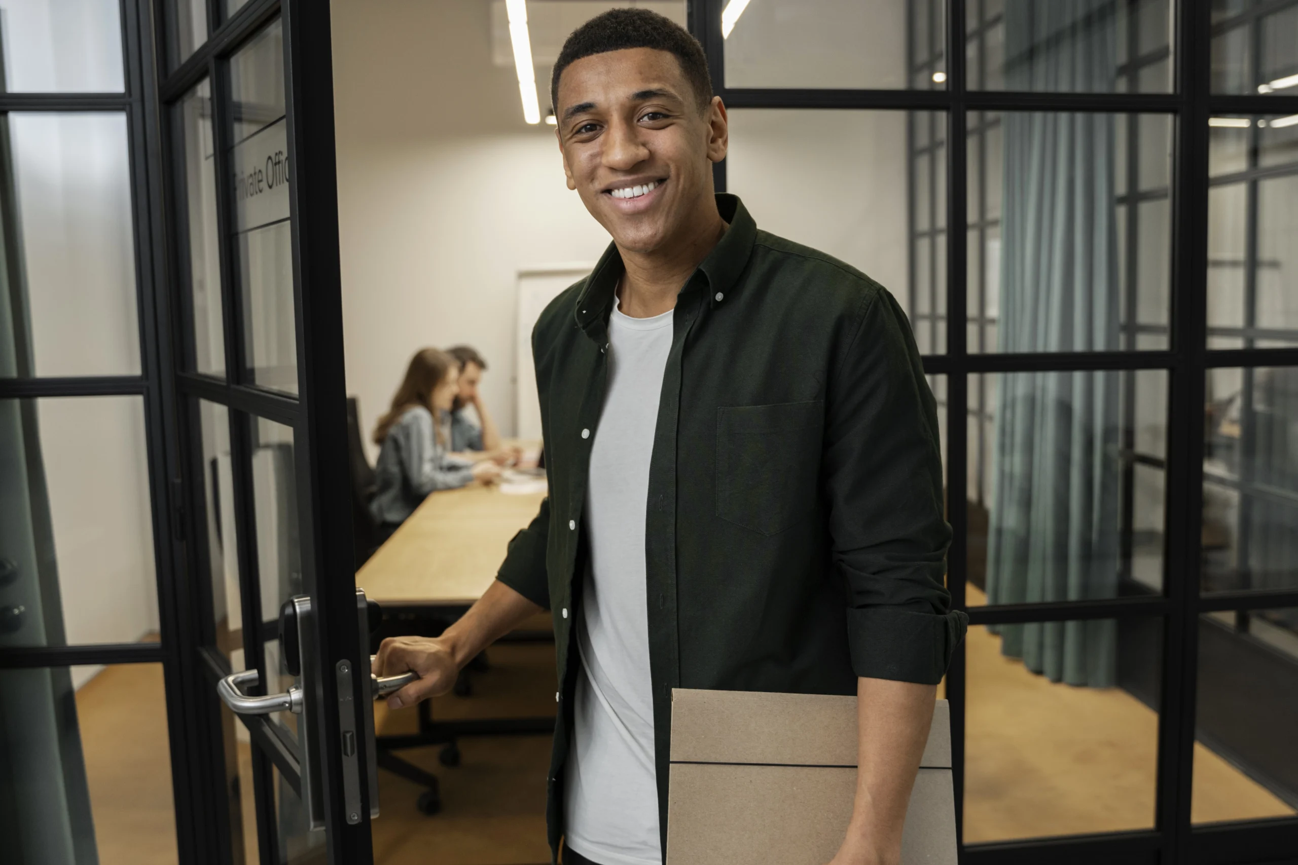 Programa Jovem aprendiz, na imagem um rapaz sorridente abrindo uma porta de vidro para ingressar em uma reunião com seus colegas.