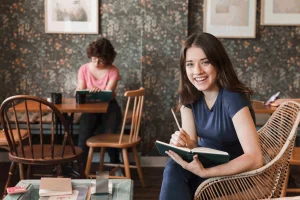 Jovem sentada com caderno aberto e escrevendo, sorrindo