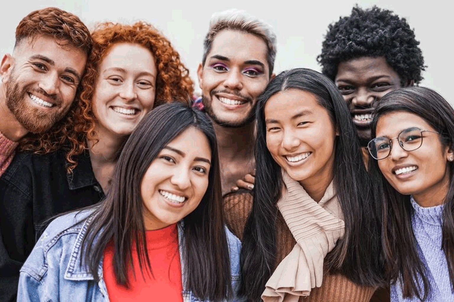 Na foto jovens de grupos diversos sorriem, temos pessoas brancas, ruivas, amarelas, negras, homossexuais, altas e baixas, homens e mulheres.