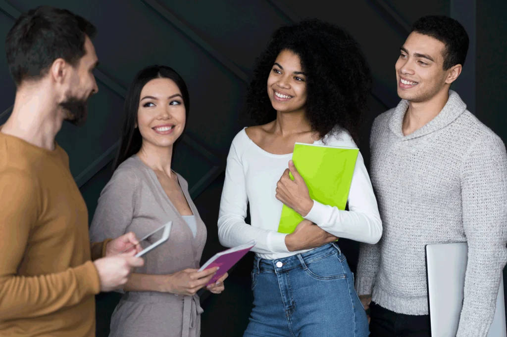 na imagem quatro jovens sorriem e conversam, aparentemente estão em uma reunião de trabalho ou em uma entrevista para vagas.