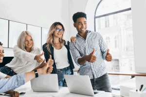 Na imagem estagiários sorriem! São 4 estagiários, 3 jovens mulheres e 1 rapaz, sorrindo e fazendo joinha com as mãos para foto.