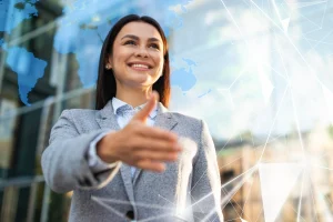 Mulher de negócios sorridente estende a mão para um cumprimento, simbolizando networking, parceria profissional e confiança no ambiente corporativo. Fundo com elementos de tecnologia e mapa do mundo sugere conexão global e inovação no mundo dos negócios.