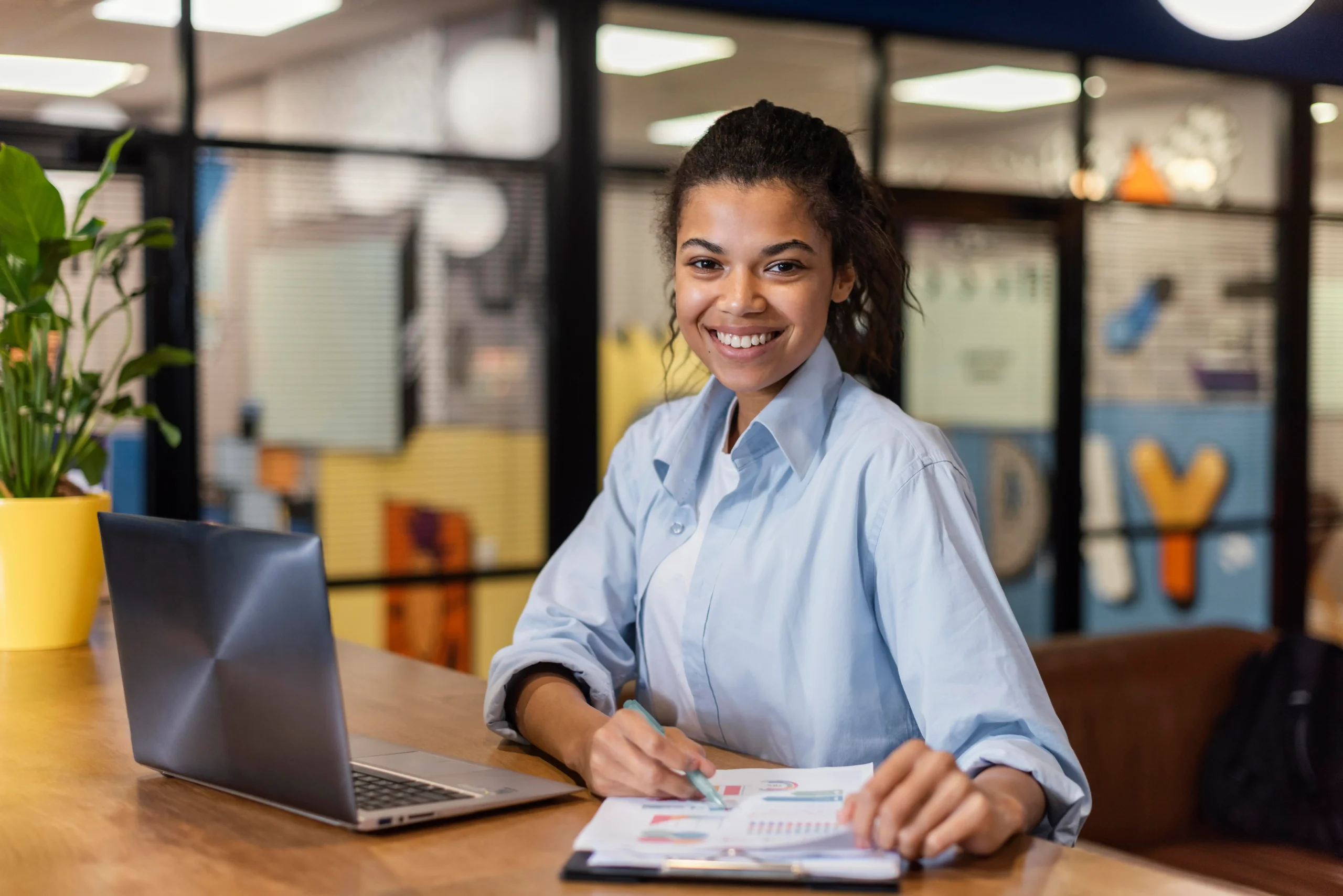 Jovem estudante em estágio remunerado com crachá e notebook em ambiente de trabalho