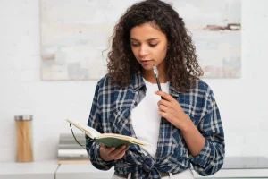 Jovem escrevendo redação do Enem com apoio de livros e materiais didáticos.
