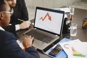 Jovem estudando em um notebook enquanto organiza livros e anotações, representando o investimento em conhecimento para crescer profissionalmente.