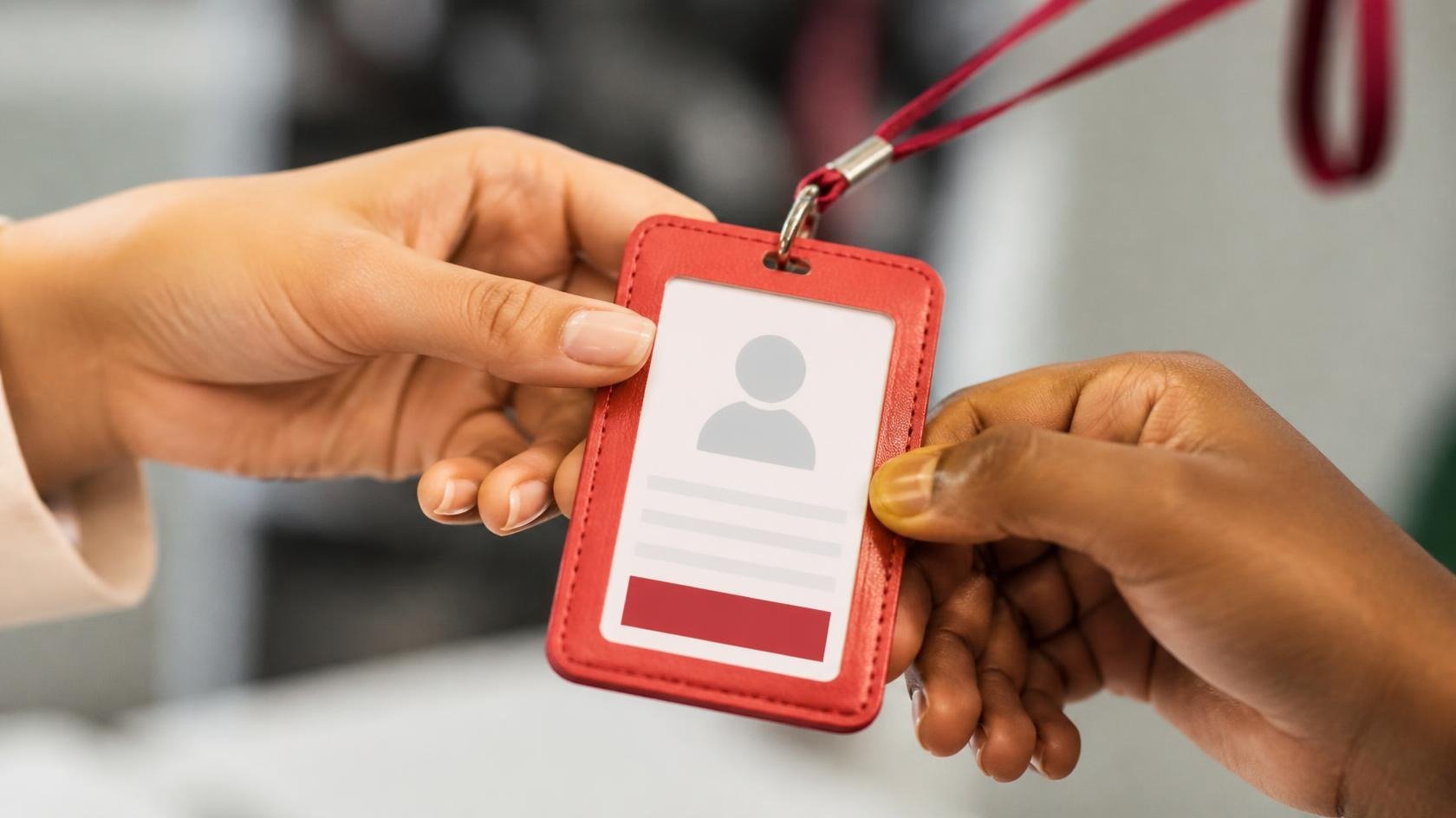 Mãos entregando um crachá de identificação vermelho, simbolizando o momento de boas-vindas de um novo jovem aprendiz