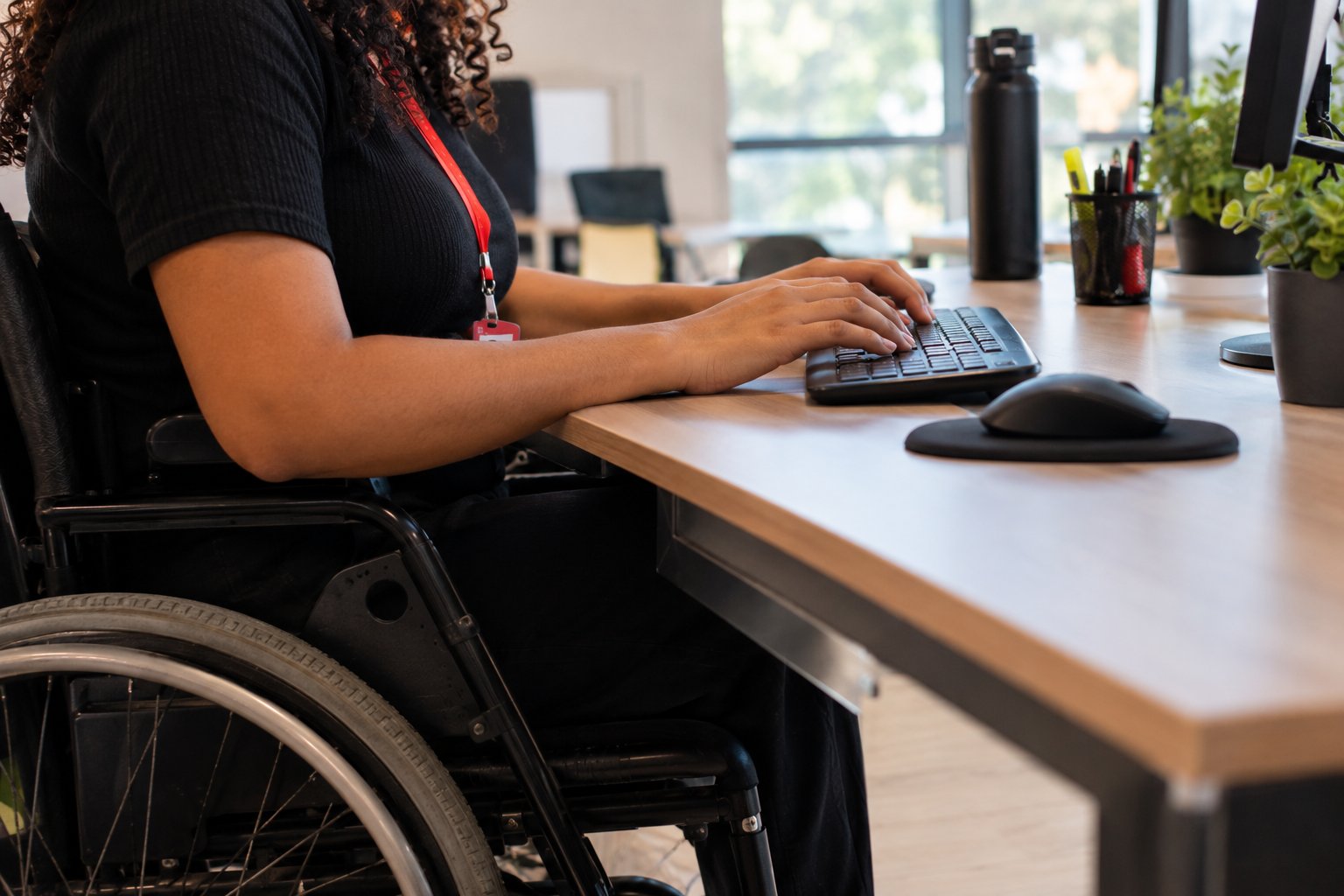 Mãos de jovem aprendiz PCD digitando em teclado durante rotina de trabalho em mesa adaptada