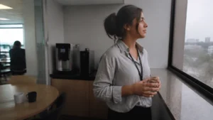 Jovem respirando fundo na copa do escritório, em uma pausa durante a ansiedade no primeiro emprego