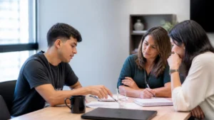 Jovem aprendiz apresentando uma ideia a duas colegas em reunião, um exemplo de como se destacar no mercado de trabalho