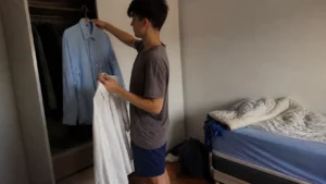 Jovem escolhendo entre duas camisas no guarda-roupa para decidir como se vestir para uma entrevista de emprego
