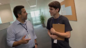 Líder conversa no corredor com jovem aprendiz, exemplo de comunicação assertiva no trabalho