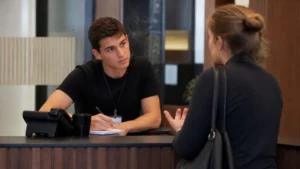 Jovem aprendiz ouve uma cliente no balcão e anota, praticando a escuta ativa na comunicação no trabalho