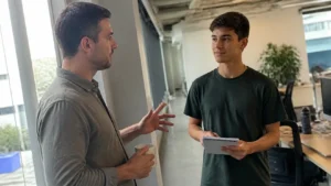 Gestor conversando com jovem aprendiz sobre feedback contínuo no corredor do escritório