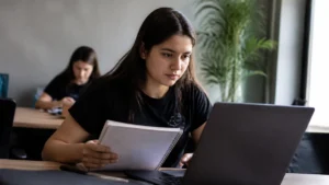 IA e o futuro dos jovens aprendizes: jovem confere anotações no caderno enquanto usa o notebook no trabalho