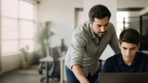 Gestor orientando jovem aprendiz em frente ao computador em ambiente de escritório