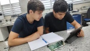 Profissões do futuro: dois jovens estudam juntos numa bancada de laboratório com uma placa eletrônica e um tablet