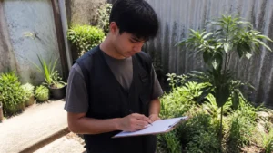 Sustentabilidade e empregos verdes: jovem anota dados numa prancheta em meio às plantas de um quintal