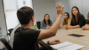 Proativo no trabalho: jovem levanta a mão para tirar uma dúvida em reunião de equipe