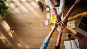 Equipe diversa reunida à mesa de trabalho discutindo estratégia, mãos gesticulando sobre anotações e notebook