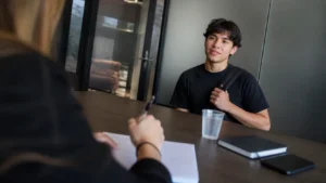 Jovem em entrevista de seleção ouve a recrutadora, exemplo de linguagem corporal na entrevista