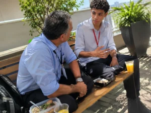 Mentoria para jovens, profissional experiente conversa com um jovem aprendiz durante o almoço em um terraço da empresa