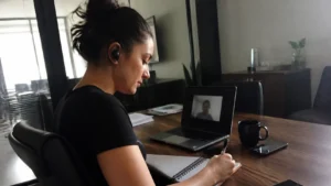 Jovem aprendiz anotando em um caderno durante uma mentoria virtual por videochamada, unindo mentoria virtual e networking estratégico