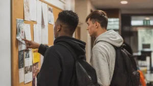 Dois jovens leem anúncios em um mural de oportunidades, buscando o primeiro passo no mercado de trabalho sem experiência