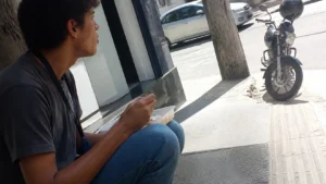 Jovem aprendiz almoçando na calçada em uma pausa do dia, dentro do prazo do contrato de aprendizagem