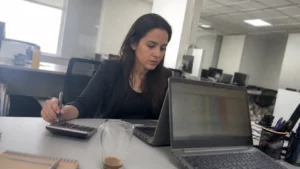 Analista de RH conferindo a folha de pagamento do jovem aprendiz com calculadora e planilha no notebook