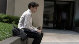Jovem sentado do lado de fora do prédio, nervoso antes da entrevista, representando a timidez na entrevista de emprego