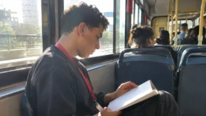 Vida de CLT, jovem com crachá lendo suas anotações no ônibus a caminho do trabalho